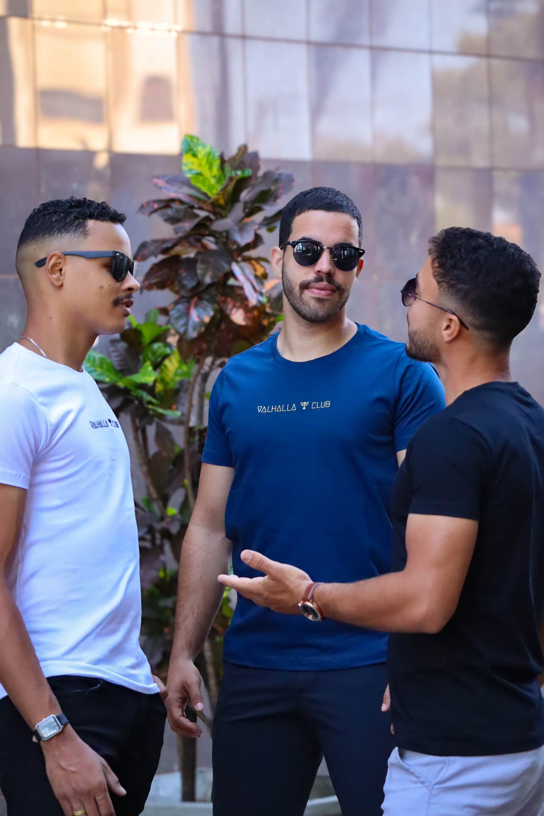 Três modelos vestindo camisetas da Valhalla Club — branca, azul e preta, estampa pequena no peito.